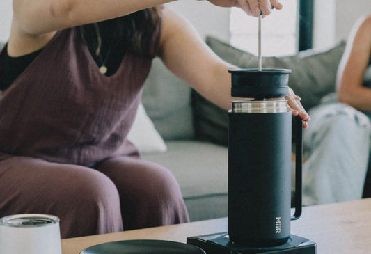 A woman making coffee using the MiiR New Standard French Press