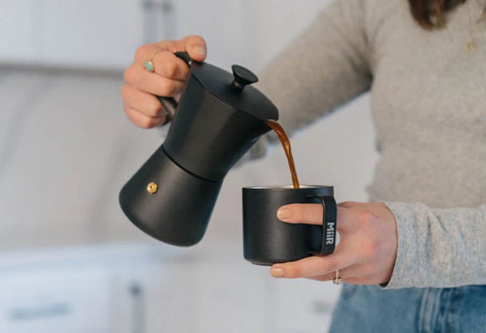 A woman making coffee using the MiiR New Standard Moka Pot
